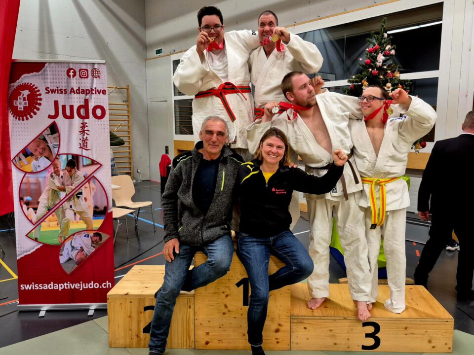 Vier ID-Judokas im Judoanzug mit Ihren zwei Coaches und den gewonnenen Medaillen auf dem Siegerpodest.